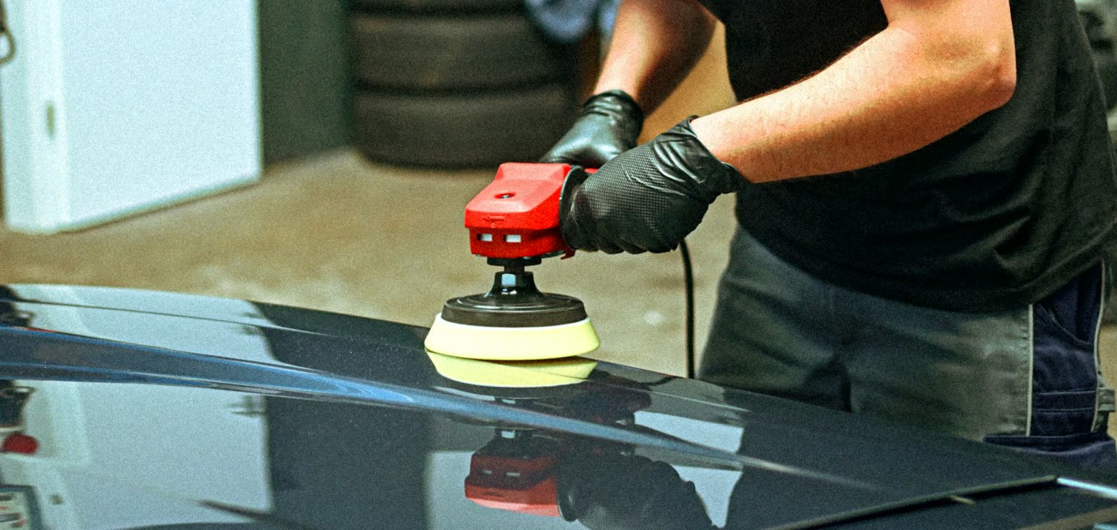 Machine polishing a black hood under shop lights